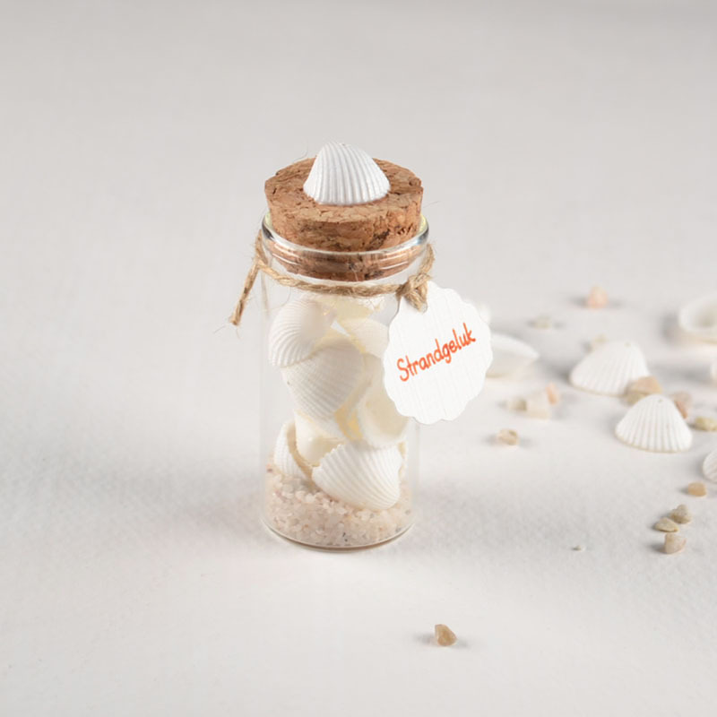 Glazen buisje met schelpjes, zand en label Strandgeluk