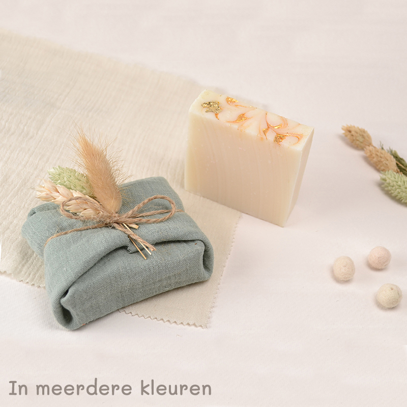 Handgemaakt zeepblok met goudaccenten en een cadeauverpakking in groen linnen, versierd met droogbloemen en jute touw.