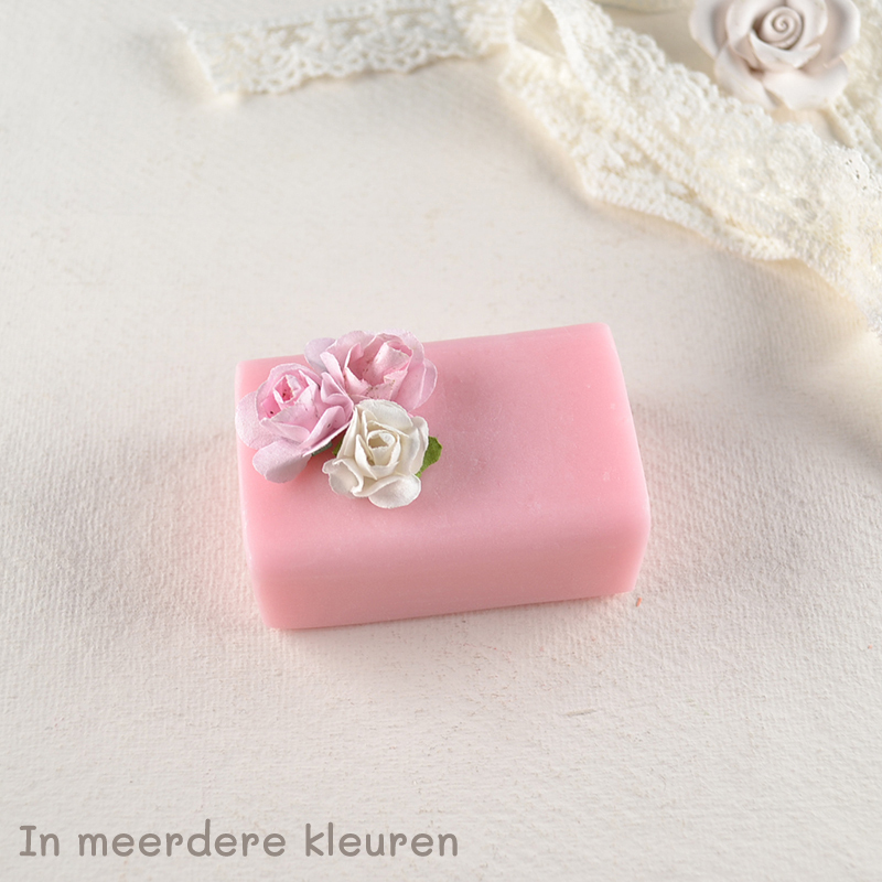 Lichtroze gastenzeepje met decoratieve papieren roosjes en kanten lint op een lichte ondergrond.