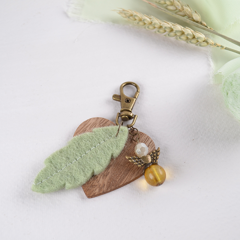 Bronskleurige hanger met houten hartje, groene vilten veer en engeltje van kralen – naturel boho stijl
