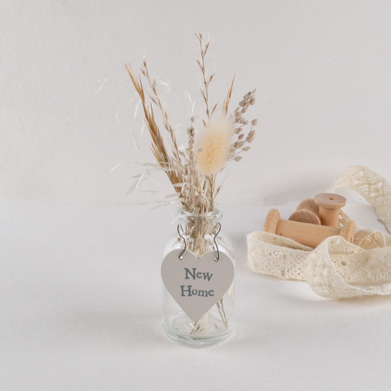 Klein glazen vaasje met droogbloemen en een hartvormig New Home label