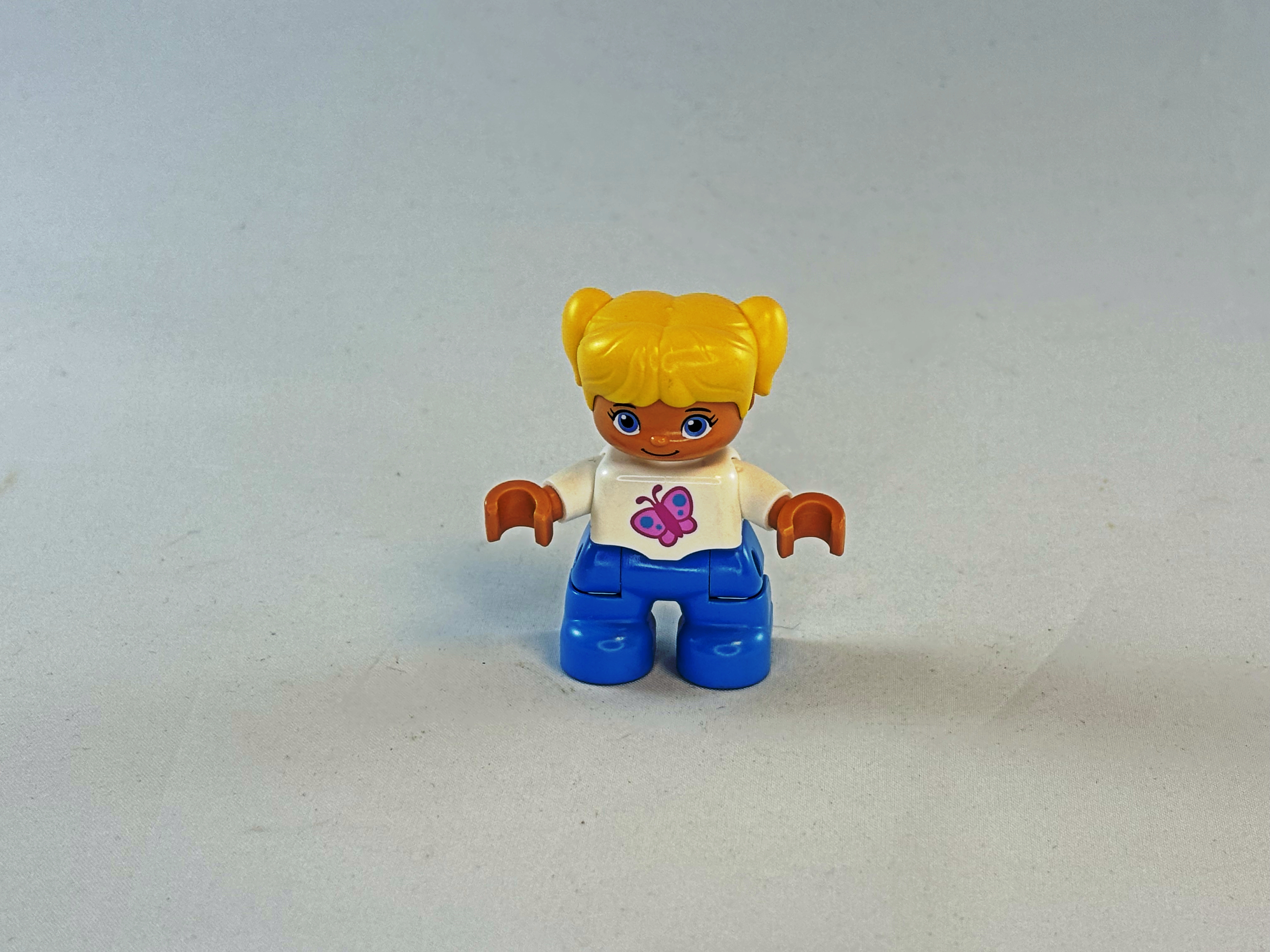 Meisje met blauwe broek, wit shirt met vlinder erop en geel haar Duplo