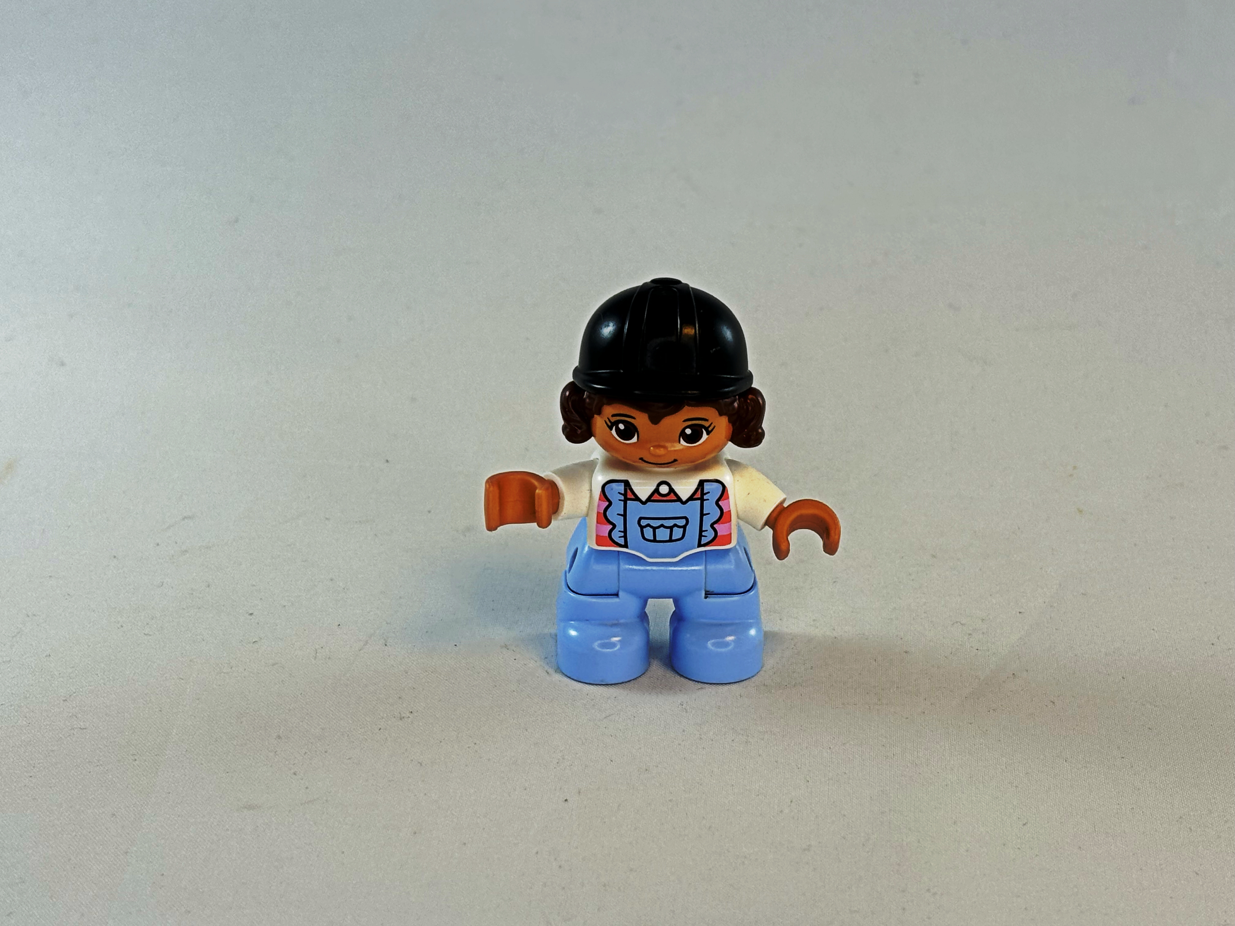 Meisje met licht blauwe tuinbroek, wit shirt, cap en bruin haar Duplo