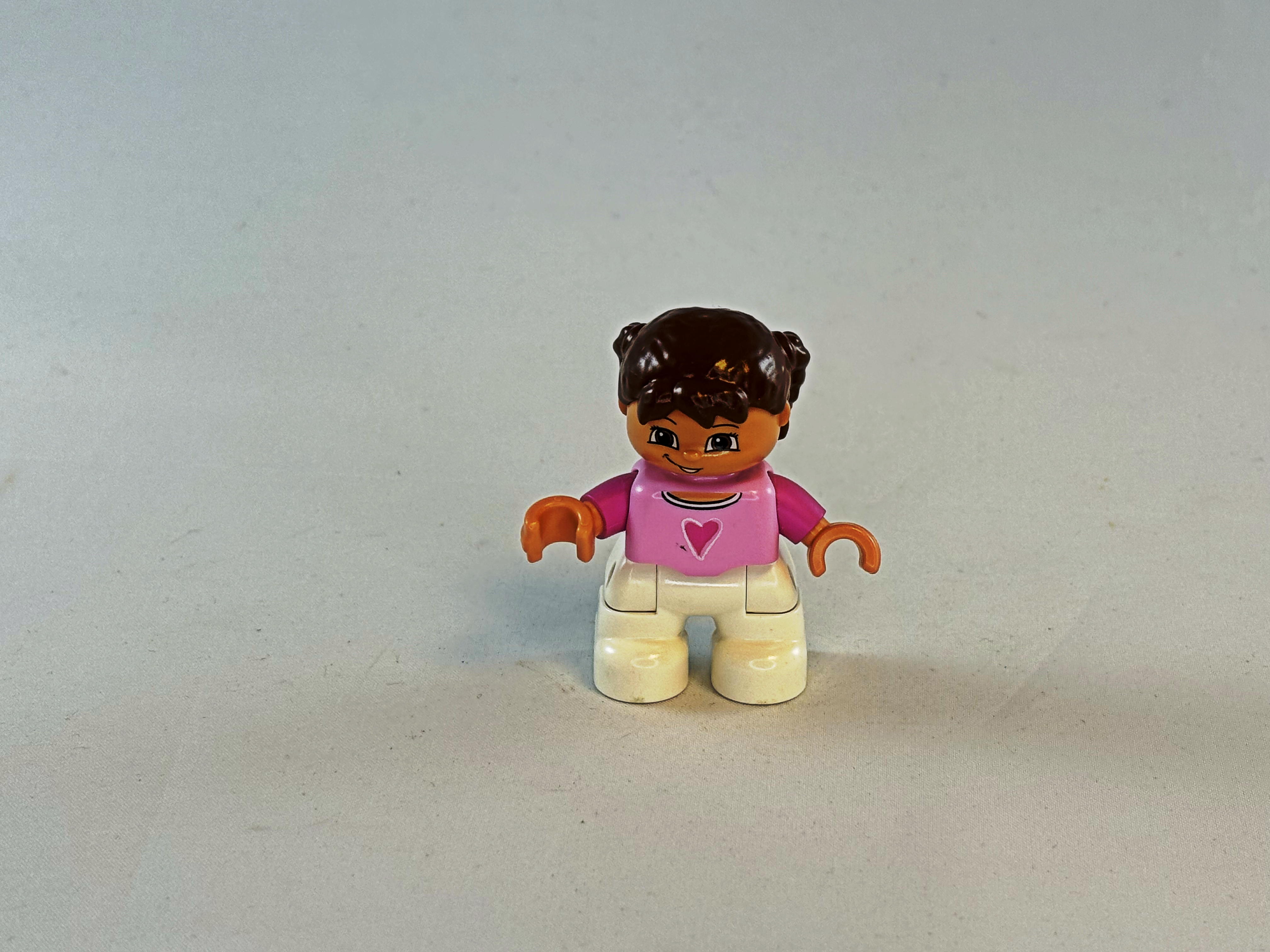 Meisje met witte broek, roze shirt met hartje erop en bruin haar Duplo