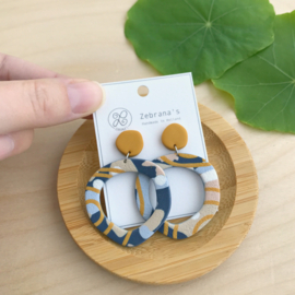 Organisch ronde statement oorbellen met abstract patroon in navy en okergeel, handgemaakt van klei (met rvs oorstekers)