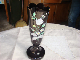 Zwarte glazen vaas op voet met geschilderde bloemen.