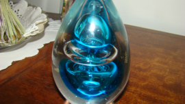 Presse-papier toren met blauwe figuur omringd met zilverkleurige ring om instulping figuur.