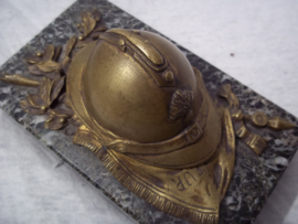 Press-papier, French miniature helmet on marble base. Franse miniatuurhelm met infanterie embleem in brons, liggend op vaandel gemonteerd op een marmeren voet, zeer decoratief.