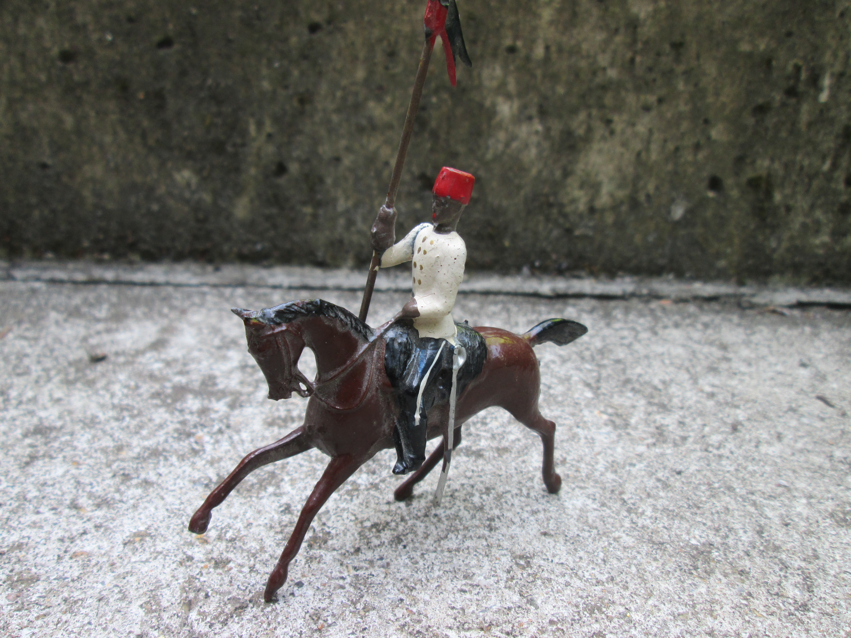 British tin toy from BRITAIN. Tinnen soldaatje koloniale ruiter met vlag bewegende arm, gemerkt.