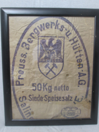 Piece of a paper bag. Stuk papier ingelijst, op de zak staat het embleem met hakenkruis van dit bedrijf. bijzonder, de rest van de zak is door muizen opgegeten.