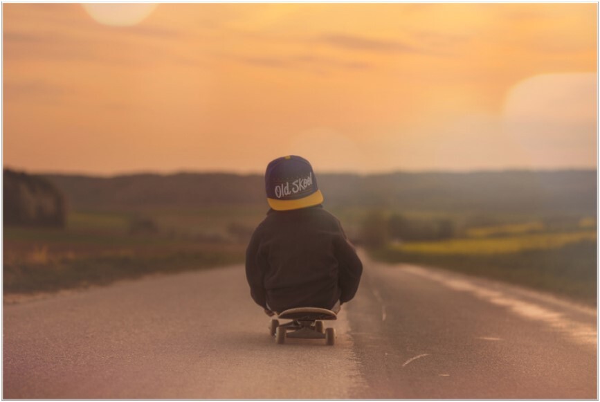 Kleine-peuter-zit-op-skateboard-rijdt-weg-van-kijker-eenzame-weg-af