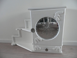 Wit houten kastje met deurtje en bewerkte spiegel, laadje en plankjes ernaast VERKOCHT