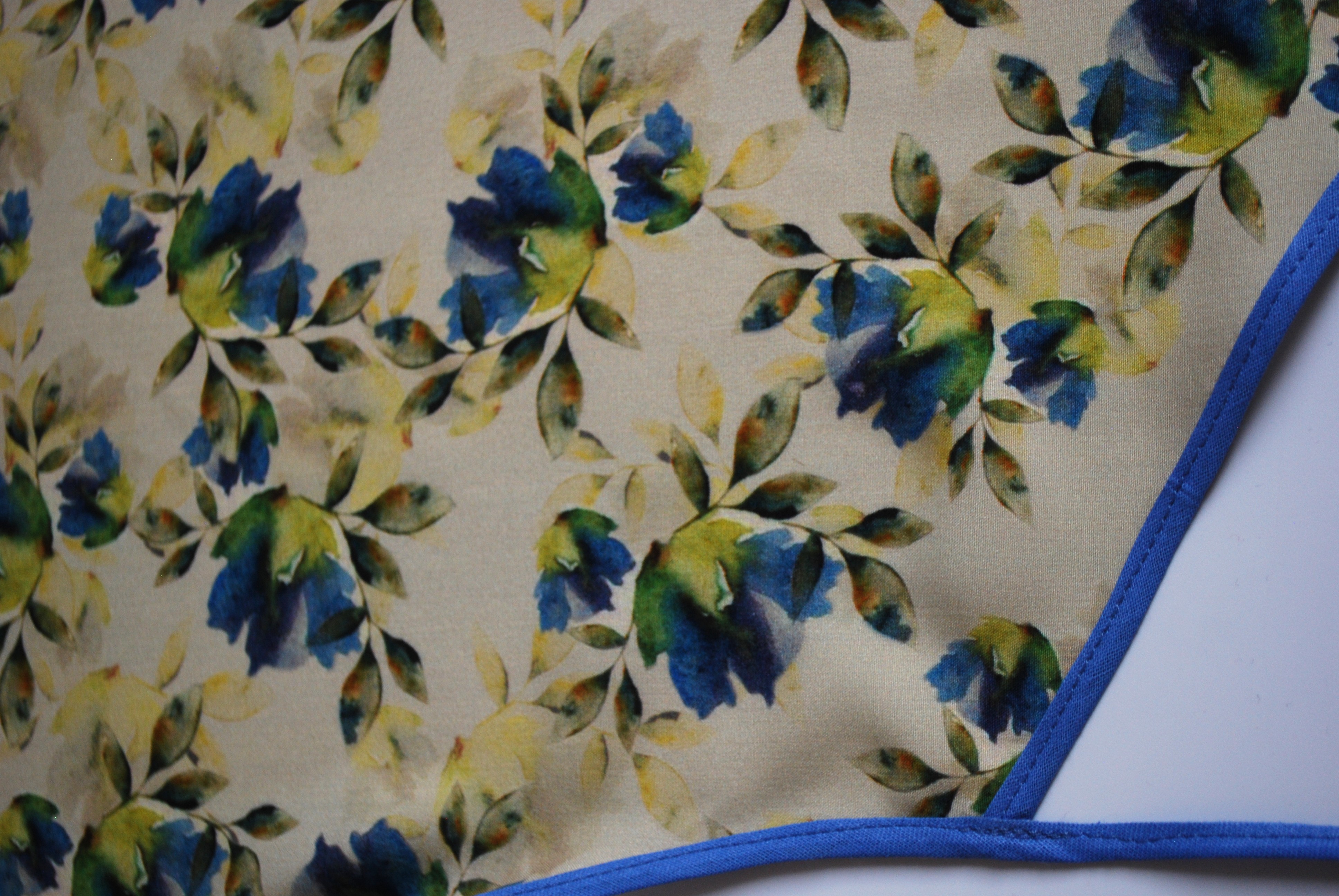 Een kapmanteltje van viscose met een boeketje van blauwe bloemen.