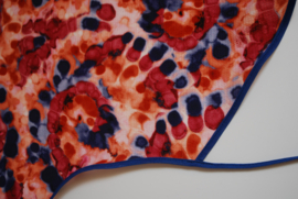 Een kapmanteltje van crêpe met een fantasie bloemmotief in de kleuren rood, oranje en blauw, met blauw biasband. Nog 1 op voorraad.