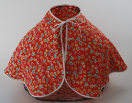 Een vrolijk, soepel vallend kapmanteltje van viscose met kleine bloemetjes op een licht rode ondergrond.