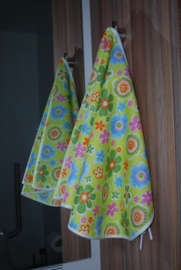 Een katoenen kapmanteltje met bloemen in diverse kleuren op een appeltjeskleurige ondergrond.