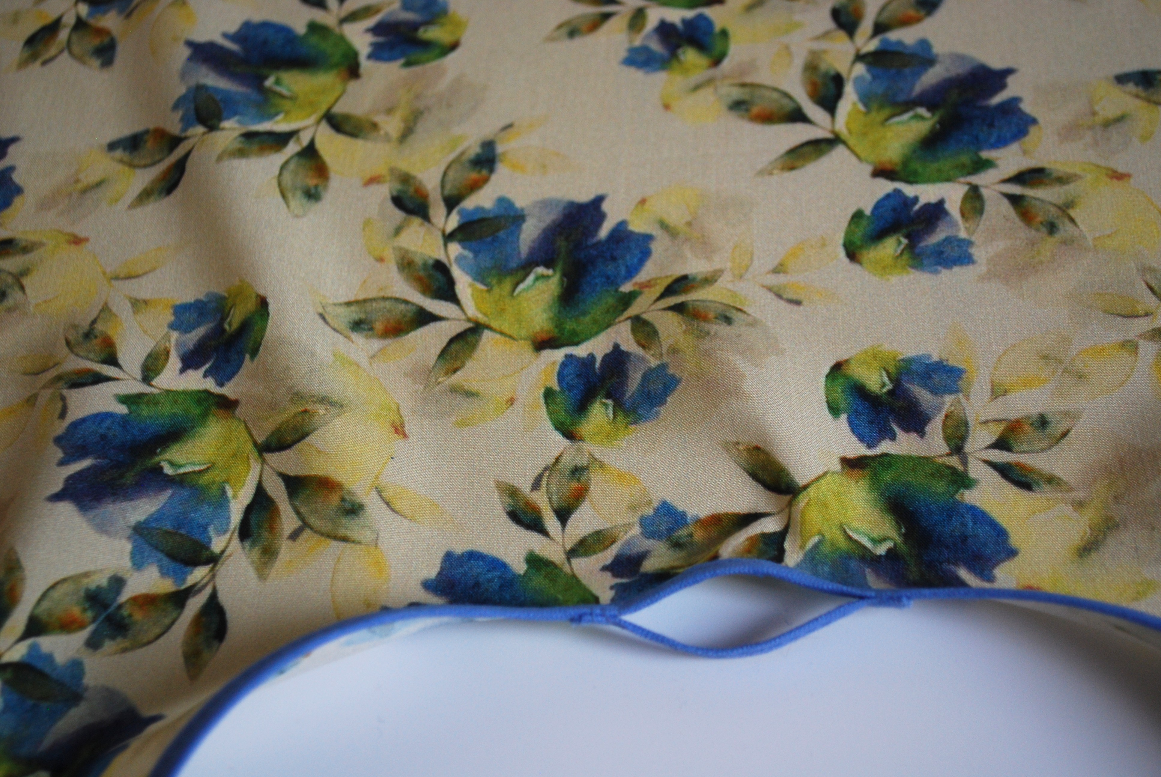 Een kapmanteltje van viscose met een boeketje van blauwe bloemen.