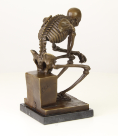 Bronzen beeld van de skelet denker op marmer basis.