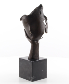 Een bronzen beeld van een gezicht dat op hand rust