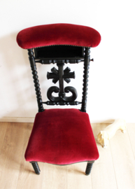 Zwarte antieke kerkstoel met rode bekleding. Vintage bidstoel / knielstoel