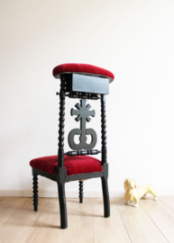 Zwarte antieke kerkstoel met rode bekleding. Vintage bidstoel / knielstoel