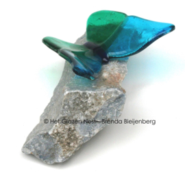 Blauwgroene glazen vlinder op blauwe steen