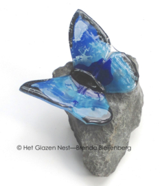 Blauwe glazen vlinder op grijze steen