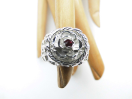 Zilveren bloem op piet-piet ring met rood steentje.