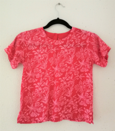 Lief shirtje van batik in roze tinten. Met mouwtje en zijsplitjes. Sluit met knoopje achter. Maat 140-146. 100% rayon.