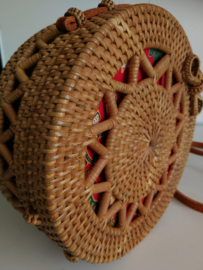 Meesterlijk vlechtwerk dit opengewerkte rotan tasje. Prachtig afgewerkte sluiting; draagband van bruin leer. Lengte band 1.27 cm. Sluit met sierlus. Diameter 20 cm, 8 cm diep.