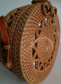 Meesterlijk vlechtwerk dit opengewerkte rotan tasje.  Prachtig afgewerkte sluiting; draagband van bruin leer. Lengte band 1.25 cm. Sluit met sierlus. Diameter 20 cm, 8 cm diep.