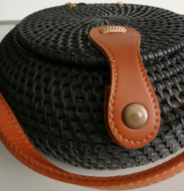 Zwart rotan bol tasje.  Subliem afgewerkte sluiting en draagband van bruin leer. Lengte band 1.23 cm. Sluit met stevige drukknoop. Diameter 20 cm, 10 cm diep.