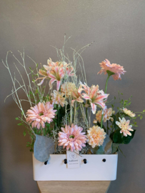 Witte vaas met stokjes met roze, zalme en grijze tinten